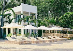 Un complexe hĂŽtelier situĂ© en bord de mer, dotĂ© de chaises longues, de parasols et dâun bĂątiment moderne.