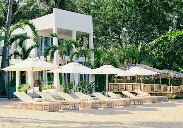 Un complexe hĂŽtelier situĂ© en bord de mer, dotĂ© de chaises longues, de parasols et dâun bĂątiment moderne.