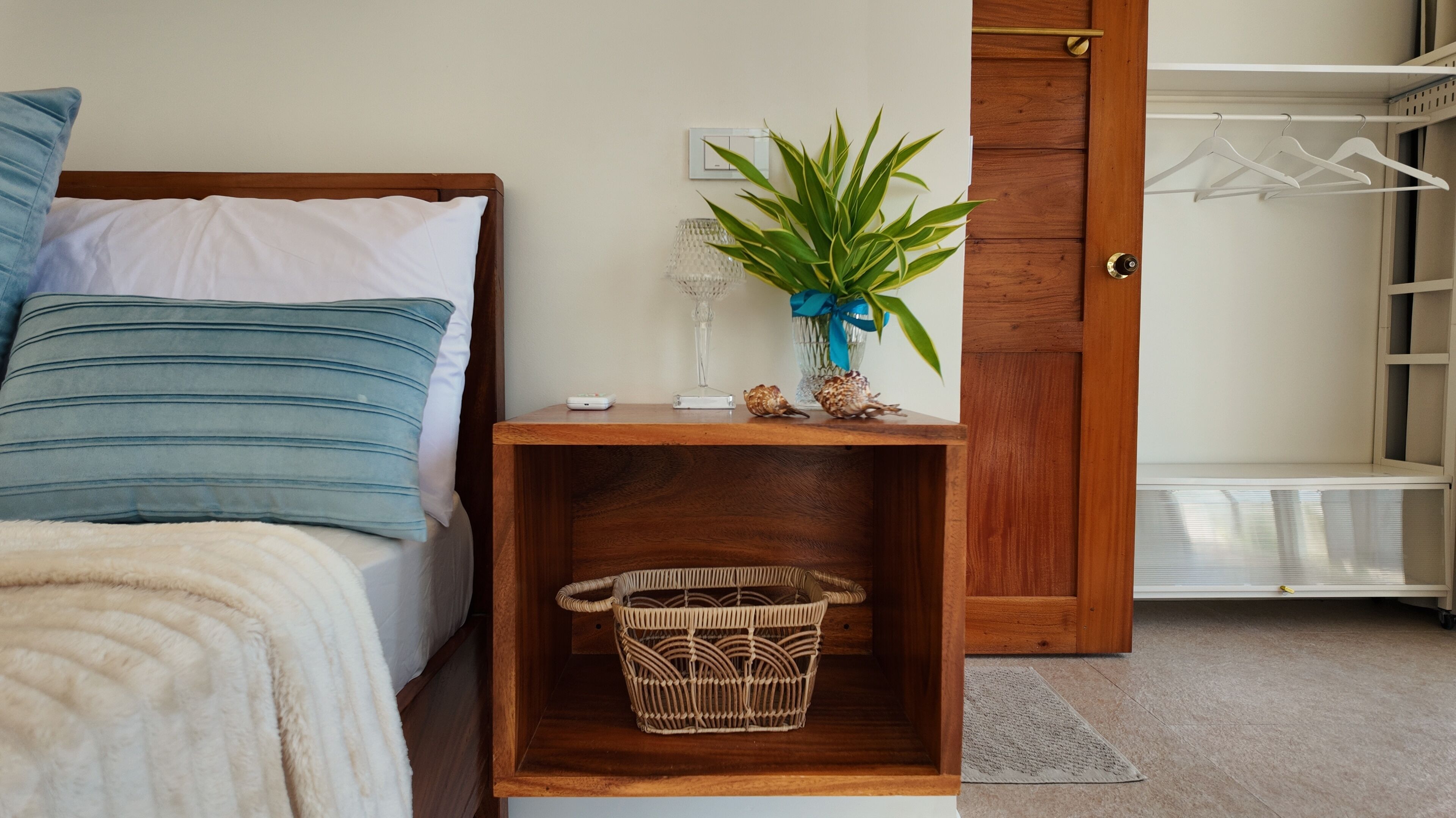 Une chambre à coucher avec un lit, une table de chevet, une plante et une armoire en bois.