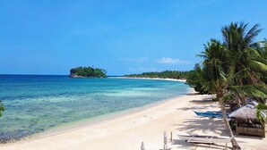 A beach with clear turquoise water, a sandy shore, and a small island in the distance.