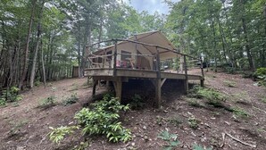 A wooden cabin with a deck, surrounded by a forest. - Off-Grid Glamping Retreat | 180 Private Acres (Lenoir)