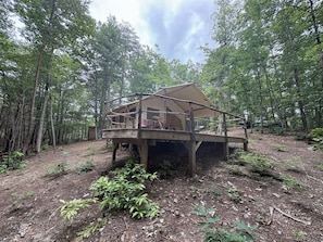 A wooden cabin with a deck, surrounded by a forest.