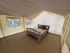 A tent with a bed, two windows, and a view of trees.