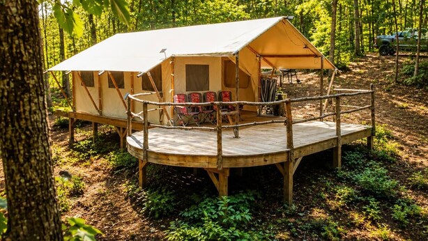 A forested campsite with a large tent and a wooden deck. - Off-Grid Glamping Retreat | 180 Private Acres (Lenoir)