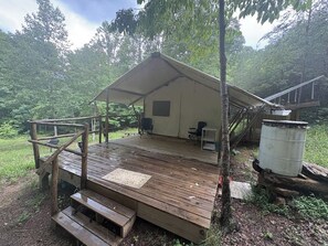 Une cabane rustique dotĂ©e dâune terrasse en bois, dâun espace salon couvert et dâun grand rĂ©servoir dâeau.