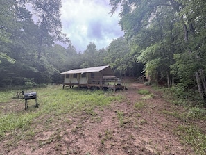 A rustic cabin with a porch, surrounded by dense forest.