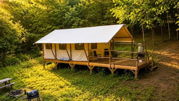 Una carpa con una terraza de madera, una parrilla y una mesa de picnic en un bosque.