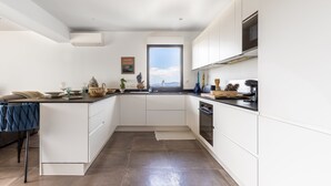 A modern kitchen with white cabinets, a built-in oven, and a window overlooking the sky. - Fiore di Macchja - À 5 min à pied de la plage (Albitreccia)