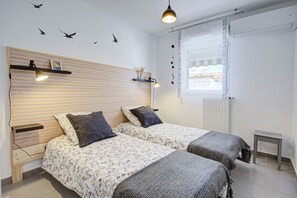 A bedroom with two beds, a wooden headboard, a small table, and a window with blinds. - Mer & Lumière Banyuls - Appt à 600m de la plage (Banyuls-sur-Mer)