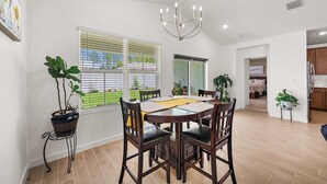 A dining area with a table, chairs, and a chandelier. There is a window with blinds, a potted plant, and a view of the outside. - Spacious Modern Villa with Private Yard, Ocala (Ocala)