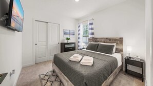 A bedroom with a bed, a nightstand, a TV, a door, and a window with curtains. - Spacious Modern Villa with Private Yard, Ocala (Ocala)
