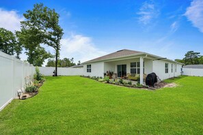 A single-story house with a covered patio, a lawn, and a white fence.