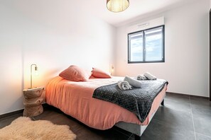 Ein modernes Schlafzimmer mit Bett, Nachttischlampe und Blick zum Himmel durch ein Fenster.