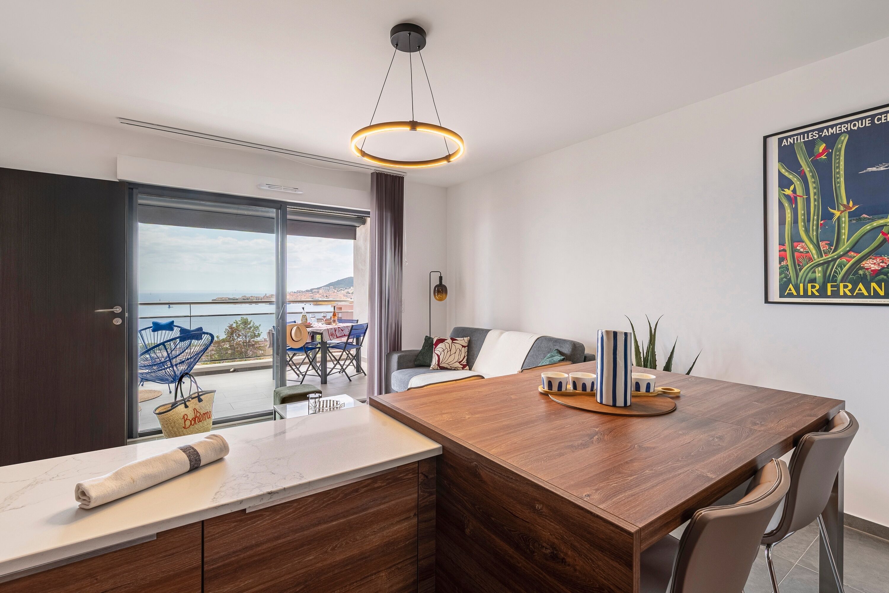 A modern kitchen with a wooden island, a dining area with a table and chairs, a large window with a view, and a ceiling light fixture.