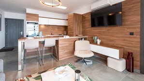 A modern kitchen with a wooden accent wall, a built-in TV, and a dining area with bar stools. - Luminella - Avec vue sur la mer (Ajaccio)