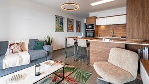 A modern living room with a sofa, coffee table, and a kitchen area with a bar. - Luminella - Avec vue sur la mer (Ajaccio)