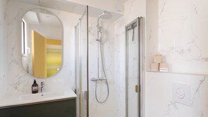 A bathroom with a glass-enclosed shower, a round mirror, and a marble wall. - Da Viken - Accès direct à la plage (Dinard)