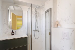 Une salle de bain avec une douche à parois de verre, un miroir rond et un mur en marbre.