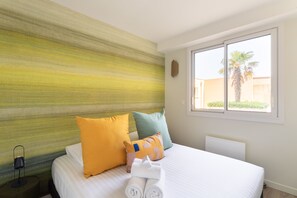 Une chambre d’hôtel avec un lit, des oreillers, une table de chevet, une fenêtre et une vue sur des palmiers.