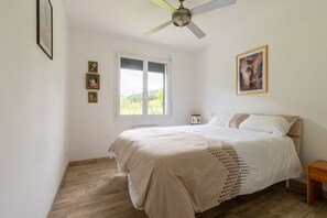 A bedroom with a bed, a ceiling fan, a window, and wall-mounted pictures.