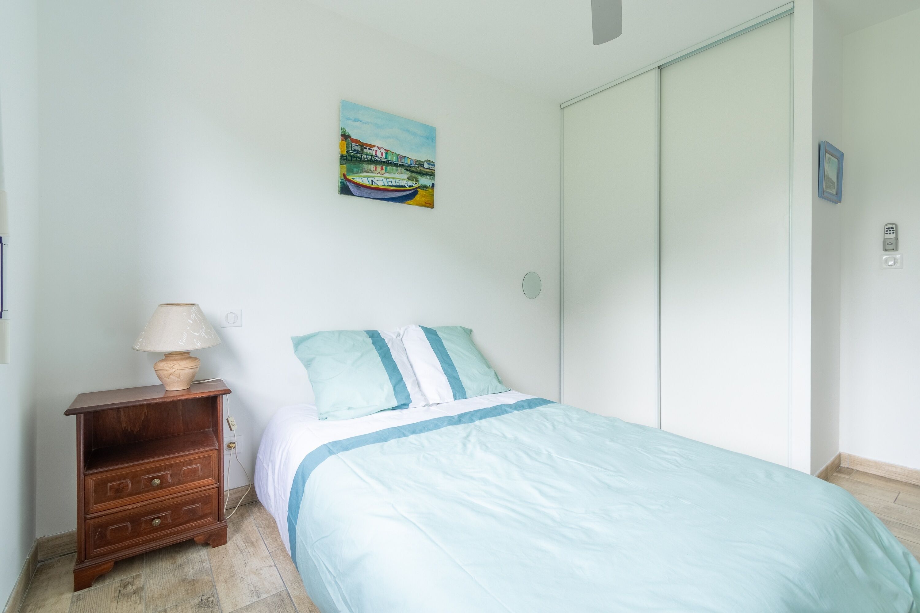 Un dormitorio con cama, una mesita de noche con lámpara, un cuadro en la pared y una puerta corredera.