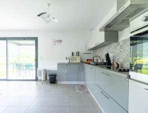 Une cuisine moderne dotée d’une porte-fenêtre coulissante donnant sur un patio, d’un four à micro-ondes, d’une bouilloire et d’un évier.