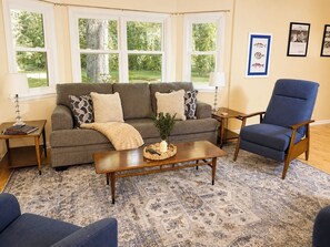 A living room with a sofa, armchair, coffee table, and a rug.