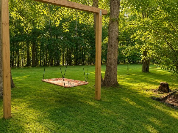 A wooden swing set in a grassy park with trees in the background.
