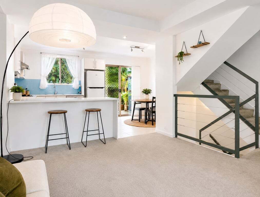 Eine moderne Küche mit Barhocker, ein Essbereich mit Tisch und Stühlen sowie eine Treppe mit Metallgeländer.
