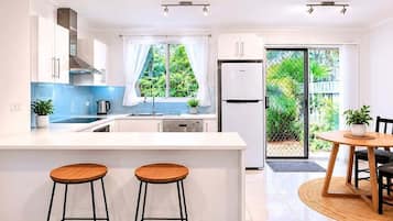 Une cuisine moderne avec des meubles blancs, un réfrigérateur en acier inoxydable et un coin repas comprenant une table ronde et deux tabourets.