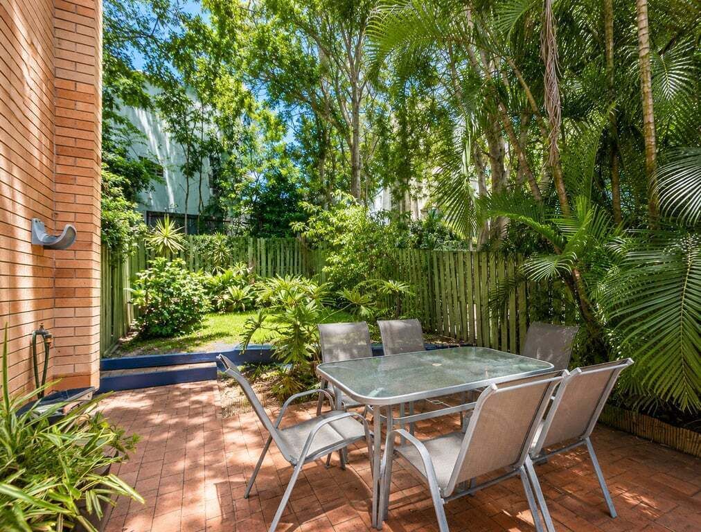 Une terrasse avec une table et des chaises, entourée d’une végétation luxuriante et d’une clôture en bois.