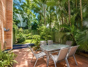 Une terrasse avec une table et des chaises, entourée d’une végétation luxuriante et d’une clôture en bois.