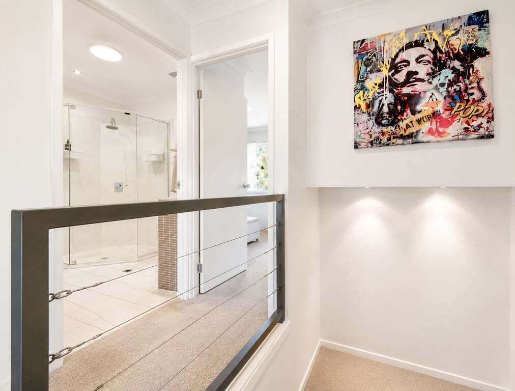 Un couloir avec une douche en verre, un mur blanc orné d’un tableau de style pop art et une rambarde en métal.