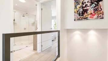 Un couloir avec une douche en verre, un mur blanc orné d’un tableau de style pop art et une rambarde en métal.