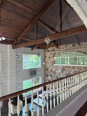 Un plafond en bois avec des poutres apparentes, un mur en pierre avec une fenêtre et une rambarde blanche.