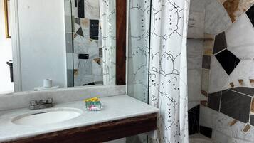 Un baño con un lavamanos blanco, un espejo, una cortina de ducha con estampado de gato y una pared de mosaicos.