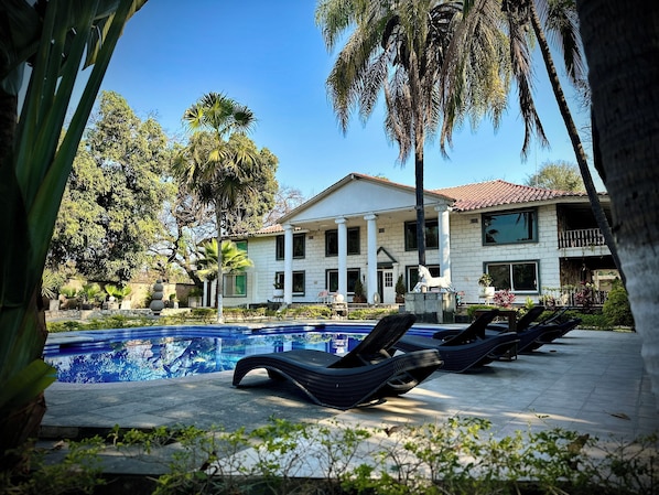 A pool area with lounge chairs, a white building with columns, and palm trees. - Casa vintage & eventos (Yautepec)