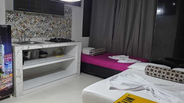 A hotel room with a bed, a TV, a desk with a sink, a ceiling light, and a window with curtains.