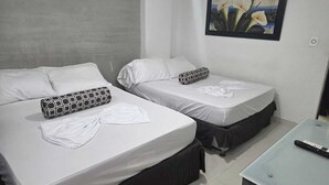 Two single beds with white linens and patterned pillows, a small table with a remote control, and a framed painting on the wall.