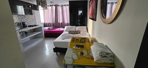Una habitación de hotel con cama, una mesita con un personaje de caricatura, una kitchenette y un baño.