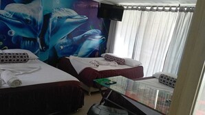 A hotel room with two beds, a glass table, a TV, and a mural of dolphins.