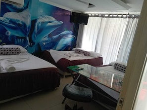 A hotel room with two beds, a glass table, a TV, and a mural of dolphins. - Apartahotel nancho rodacho (Santa marta -rodadero)