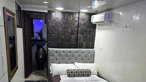 A bedroom with a bed, a white chair, a bathroom with a toilet, and a mirror.
