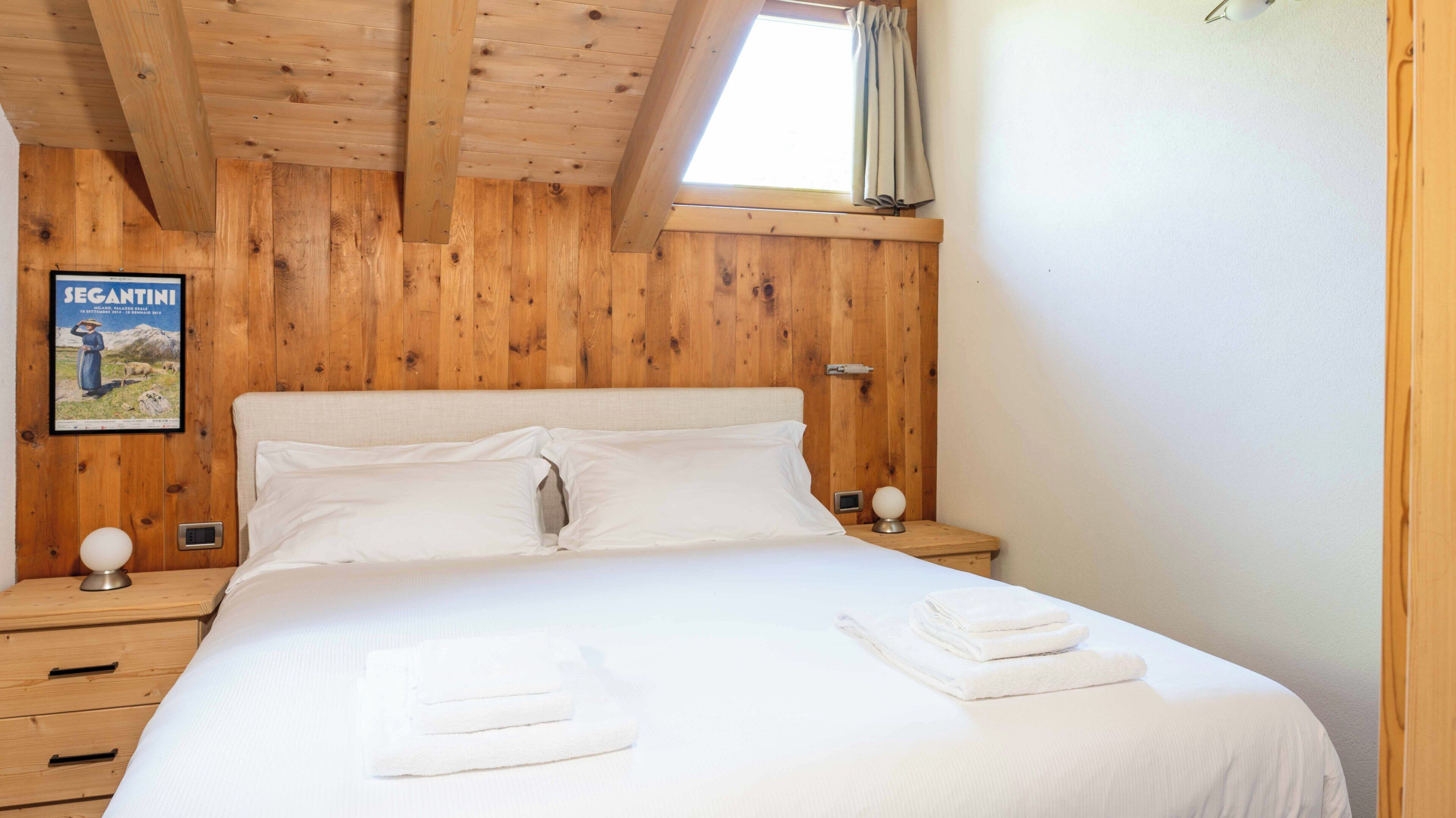 A wooden-paneled room with a bed, two bedside tables, a poster, and a window with curtains.