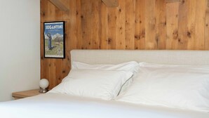 Una cama con sábanas blancas, cabecera de madera y un cartel enmarcado en la pared.