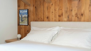Ein Bett mit weißen Leinen, einem Holzkopfteil und einem gerahmten Poster an der Wand.