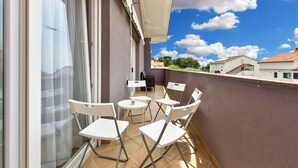 A balcony with white chairs and a small table, a sliding glass door, and a view of neighboring houses under a clear sky. - Apartment 2437/239180 (Istria - Pula), 1000m from the beach (Pula)
