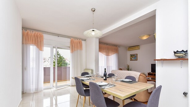 A dining area with a wooden table, four chairs, a hanging light fixture, and a view through a glass door. - Apartment 2437/239180 (Istria - Pula), 1000m from the beach (Pula)