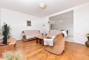 Ein Wohnzimmer mit Sofa, Sessel, Couchtisch, Fernseher und einem Blumentopf.