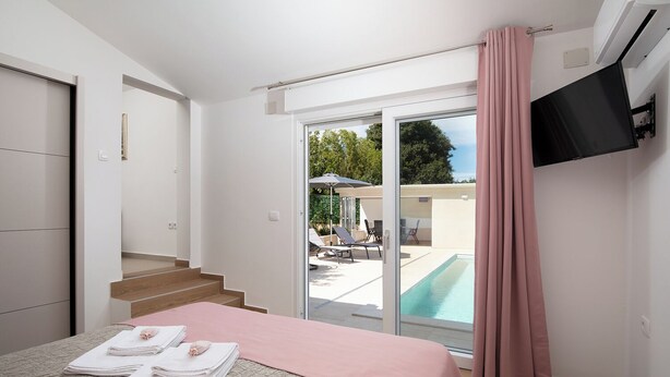 Un dormitorio con cama, televisor, puerta corrediza de vidrio a una zona de piscina y una escalera.